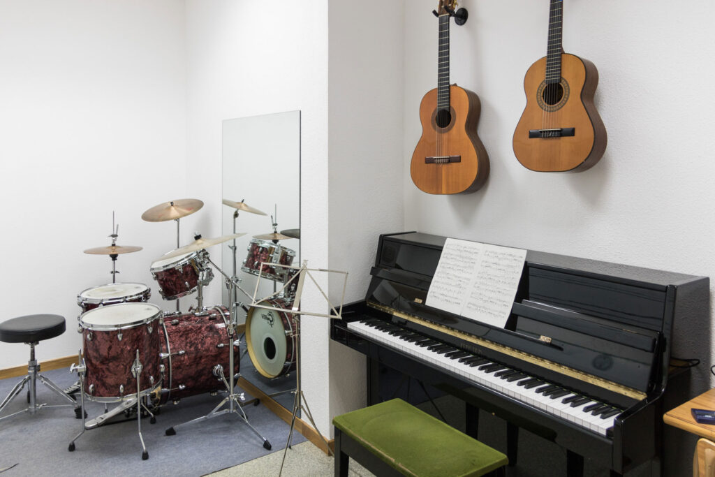 Aula con instrumentos musicales: batería, piano y guitarras.